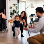 Young married couple teaching their son to learn the first baby steps in their home
